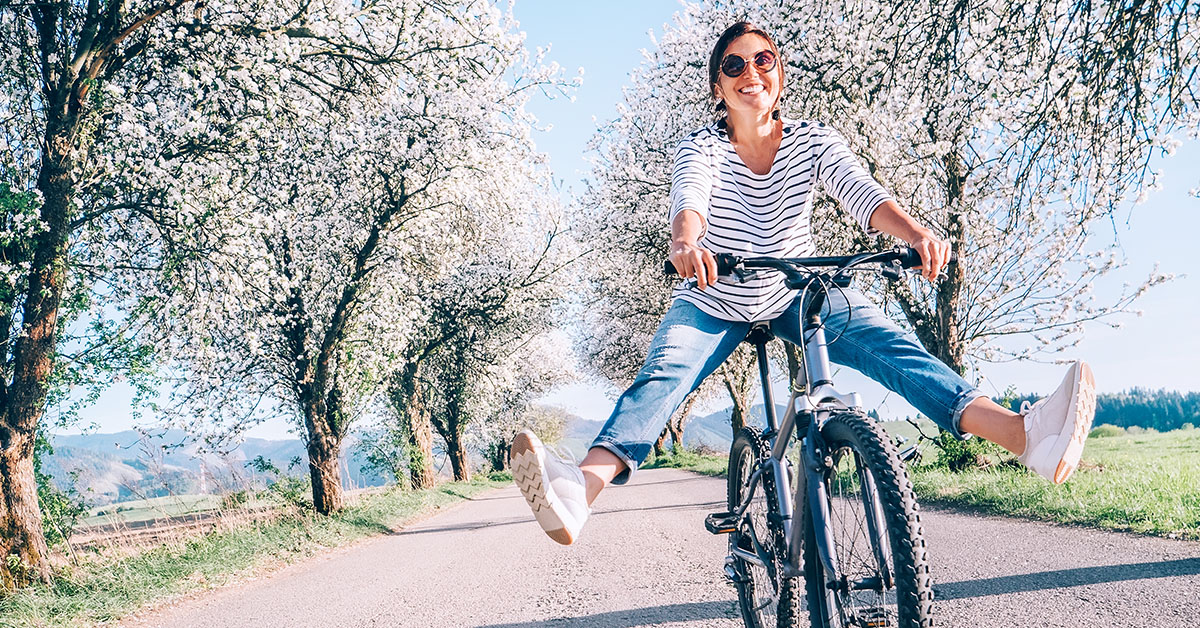 Blije, vrouwelijke, elektrische fietser op een witte fiets op een zomerse dag.