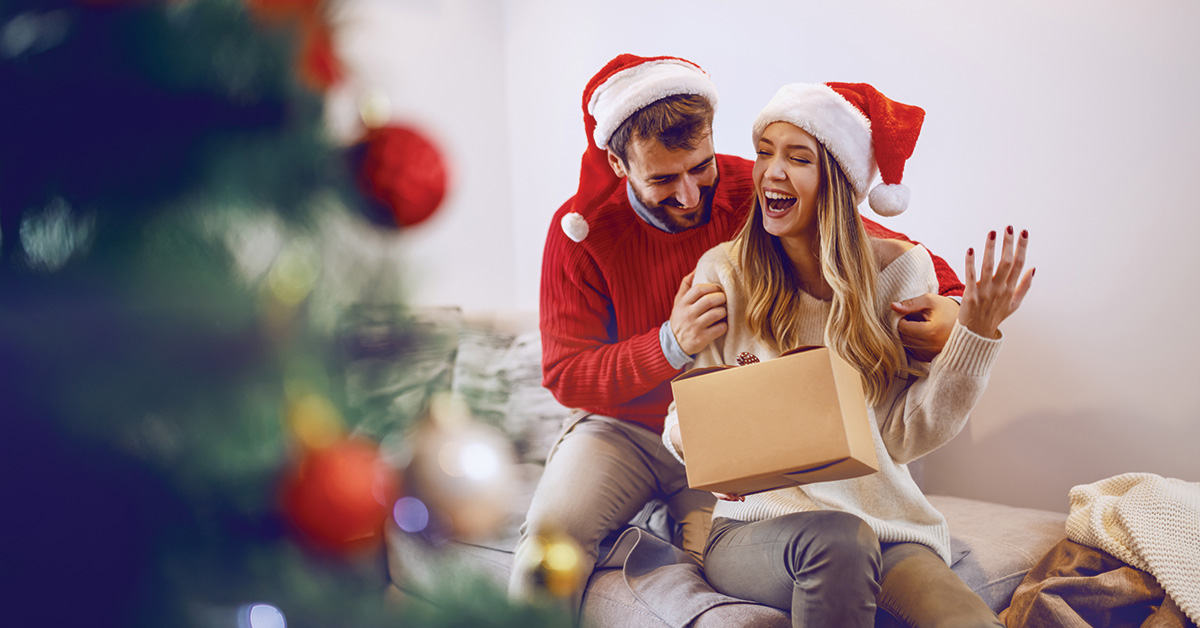 Mannelijke partner die cadeau geeft aan zijn vrouwelijke partners tijdens kerst op de bank.